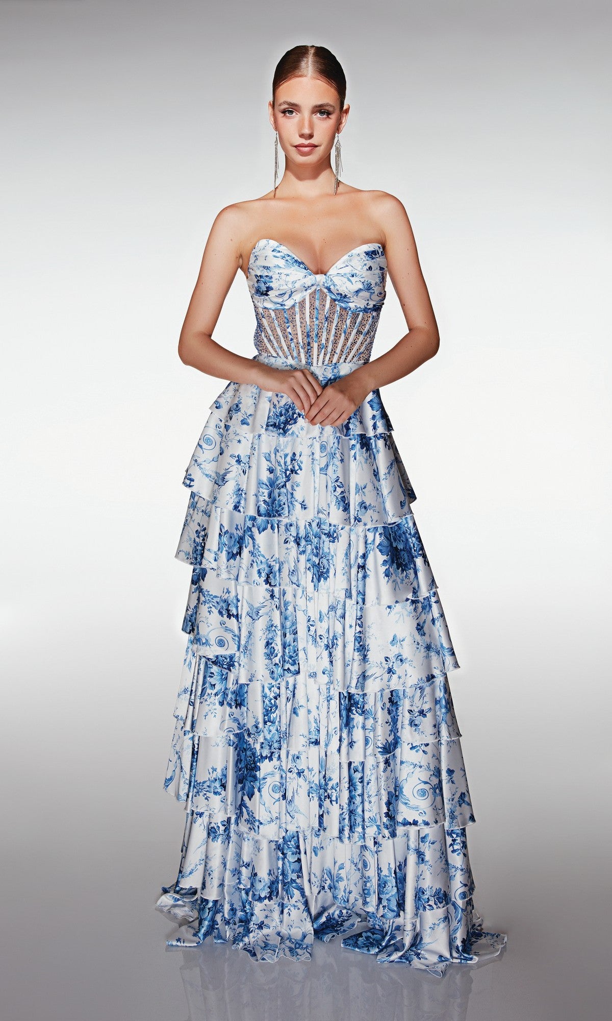 Woman modeling the Aerie Couture 374 long prom dress, featuring blue and white floral print, sheer corset bodice, and tiered ruffle A-line skirt, standing against a plain light background.